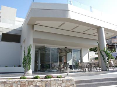 Modernes weißes Gebäude mit großer Terrasse, Glasfront und Metallstühlen bei klarem Himmel.