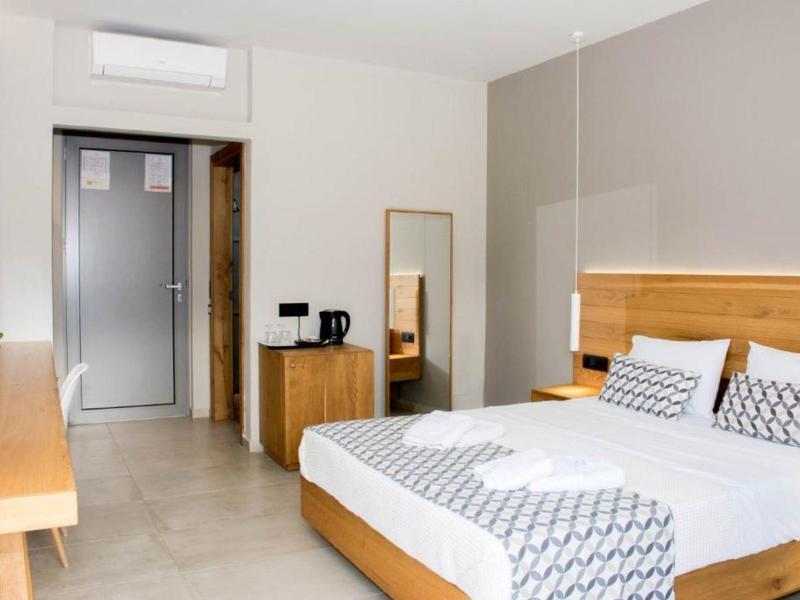 Modernes Hotelzimmer mit großem Bett, Holzmöbeln und Klimaanlage an heller Wand.