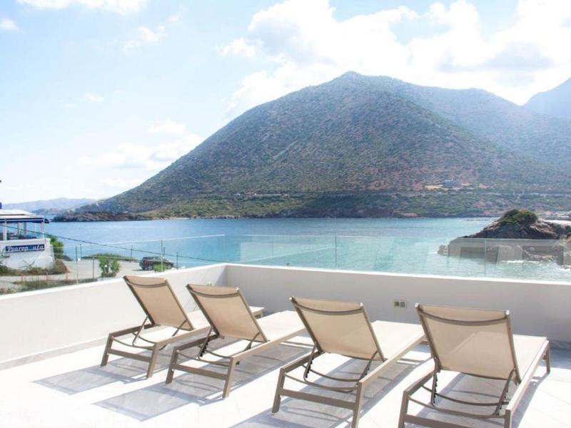 Vier Liegestühle auf heller Terrasse mit Blick auf Berg und Meer bei klarem Himmel.
