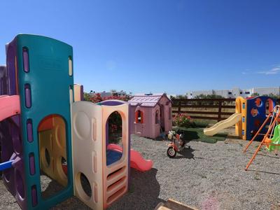 Kinderspielplatz mit zwei Spielhäusern, Rutsche, Schaukel und Fahrrad unter blauem Himmel.
