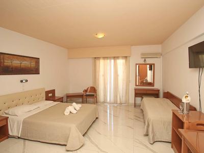 Helles Hotelzimmer mit Doppelbett, Einzelbett, Tisch, Stühlen, TV und Balkon mit Vorhängen.