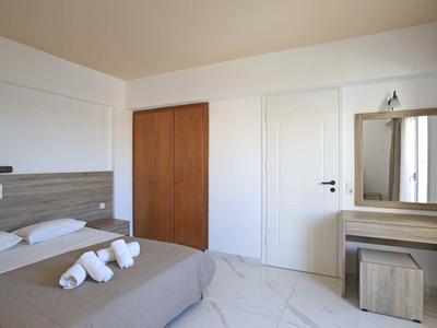 Schlicht eingerichtetes Schlafzimmer mit Doppelbett, grauer Bettdecke, Spiegel und Holzschrank.