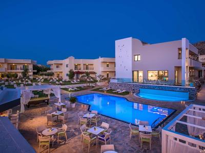 Modernes Hotel mit beleuchtetem Pool und Terrassenmöbeln bei Nacht unter klarem Himmel.