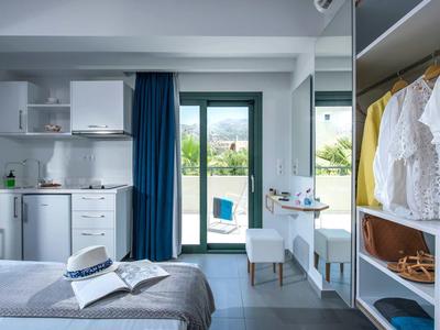 Nowoczesny pokój hotelowy z łóżkiem, otwartą szafą, małym biurkiem i balkonem z widokiem.