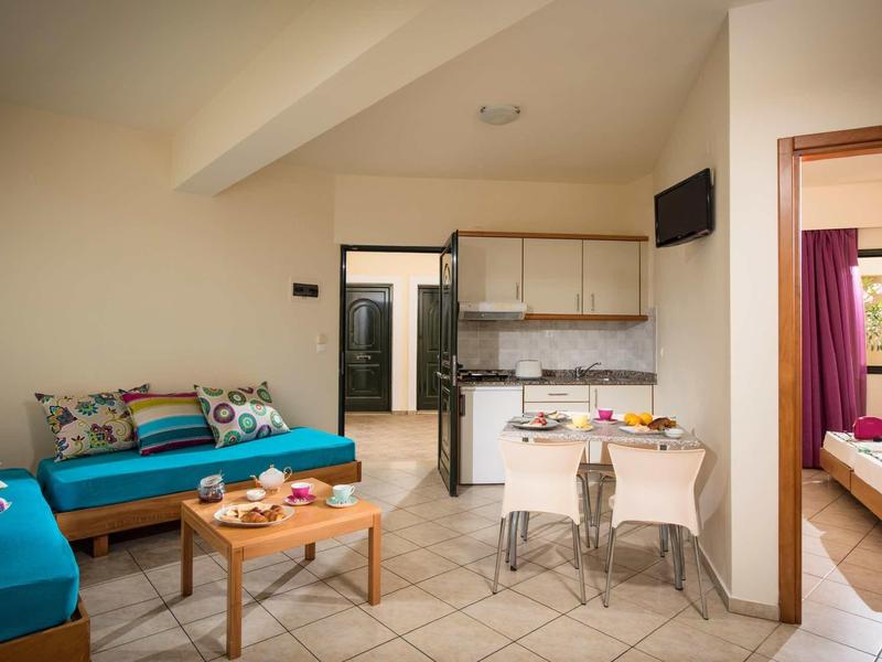 Moderne Wohnküche mit blauen Sitzbänken, Holztisch, weißen Möbeln und angrenzendem Schlafzimmer.