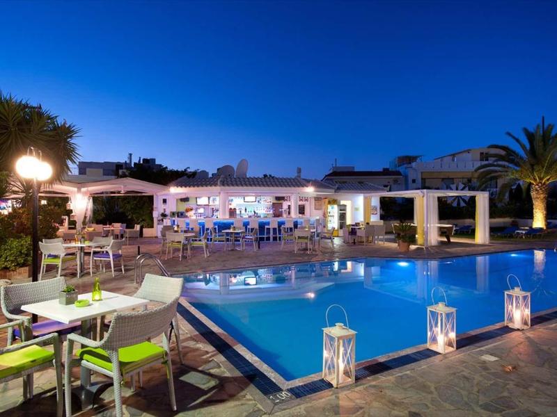 Beleuchteter Pool mit Sitzgelegenheiten, weißen Laternen und hell erleuchtetem Gebäude bei Nacht.