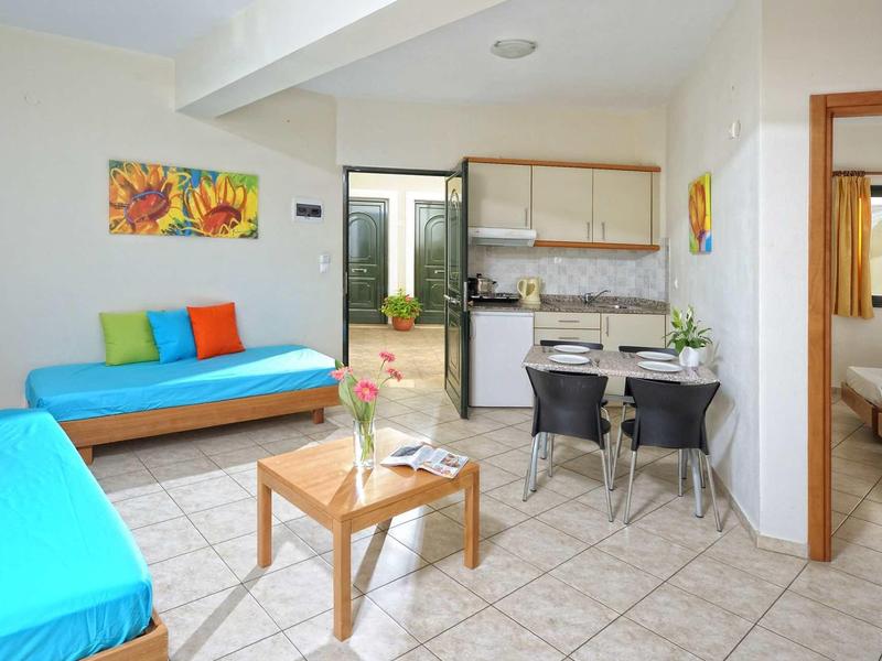 Helles Wohnzimmer mit blauen Sofas, Holztisch, moderner Küche und offenem Schlafzimmer.