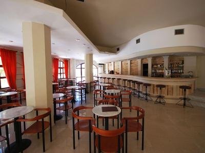 Área de bar moderna vacía con sillas y mesas de madera y una barra larga en una habitación luminosa.