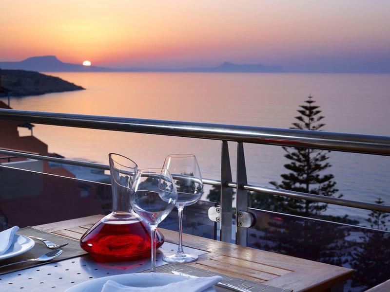 Sonnenuntergang über ruhigem Meer, Blick von Terrasse mit Gläsern und Karaffe mit rotem Getränk.