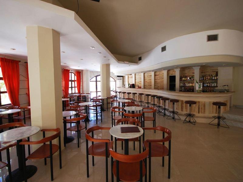 Leerer heller Barraum mit Holztischen, roten Vorhängen und langem Thekenbereich.