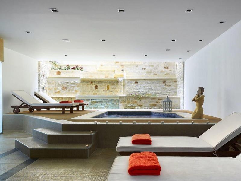 Moderner Raum mit beheiztem Pool, zwei weißen Liegen mit orangenen Handtüchern und heller Steinwand.