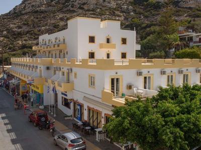 Mehrstöckiges, weiß-gelbes Gebäude an einem Berg mit Geschäften und parkenden Autos davor.