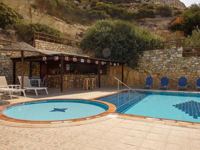 Zwei Pools mit Mosaikmustern, Holzbar und Liegestühle vor steiniger Hanglandschaft.