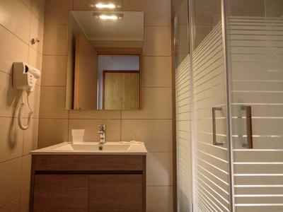 Kleines Badezimmer mit Waschbecken, Spiegel, Haartrockner und Duschkabine aus Glas.