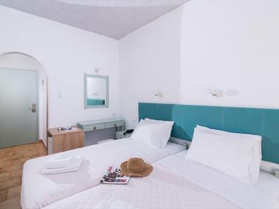 Hell eingerichtetes Zimmer mit zwei Einzelbetten, türkisfarbenem Kopfteil und schlichtem Holzboden.