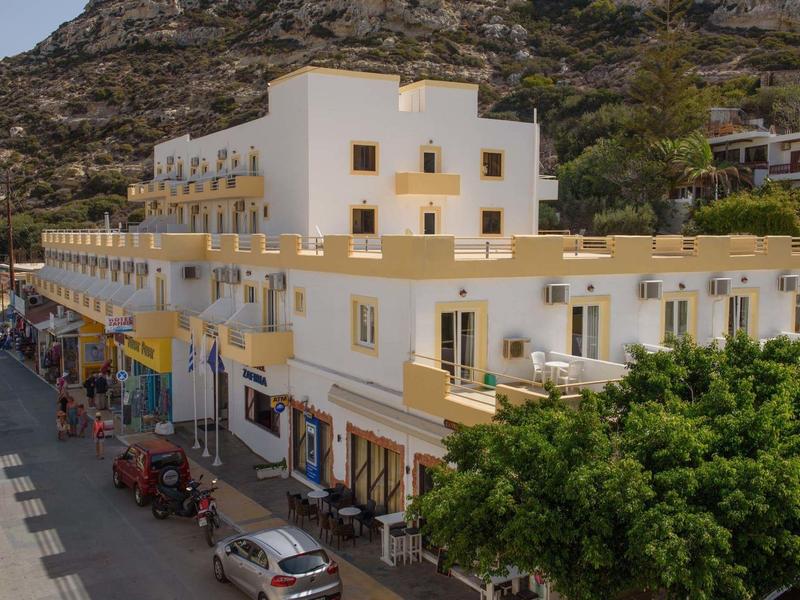 Mehrstöckiges, weiß-gelbes Gebäude an einem Berg mit Geschäften und parkenden Autos davor.