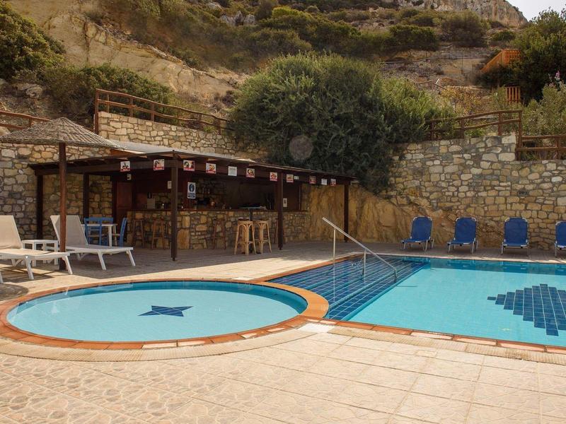 Zwei Pools mit Mosaikmustern, Holzbar und Liegestühle vor steiniger Hanglandschaft.