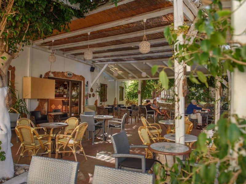 Gemütliches, offen überdachtes Café mit vielen Stühlen und Tischen, umgeben von Grünpflanzen.