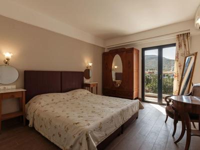 Cozy hotel room with double bed, wooden furniture, and balcony overlooking mountains.