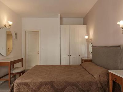 Cozy hotel room with double bed, wardrobe, mirrors, and wooden furniture under warm lighting.