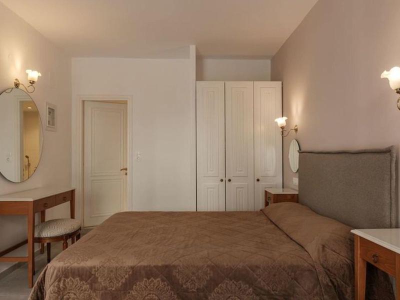 Cozy hotel room with double bed, wardrobe, mirrors, and wooden furniture under warm lighting.