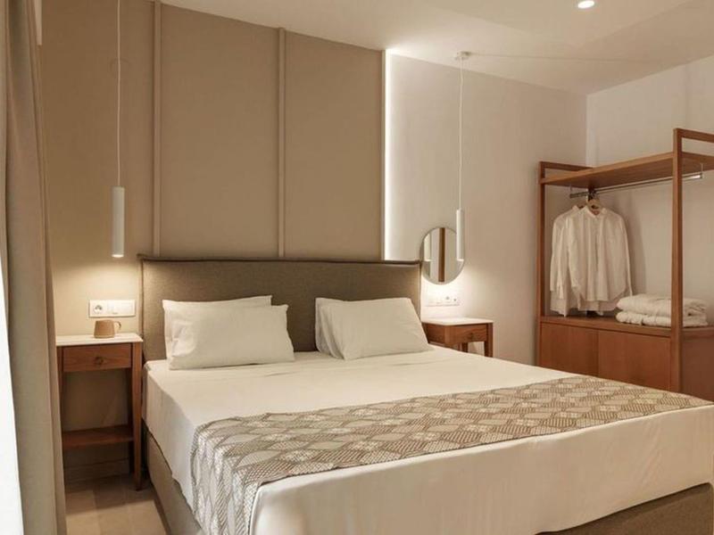 Modern hotel room with double bed, nightstands, reading lamps, and open wardrobe.