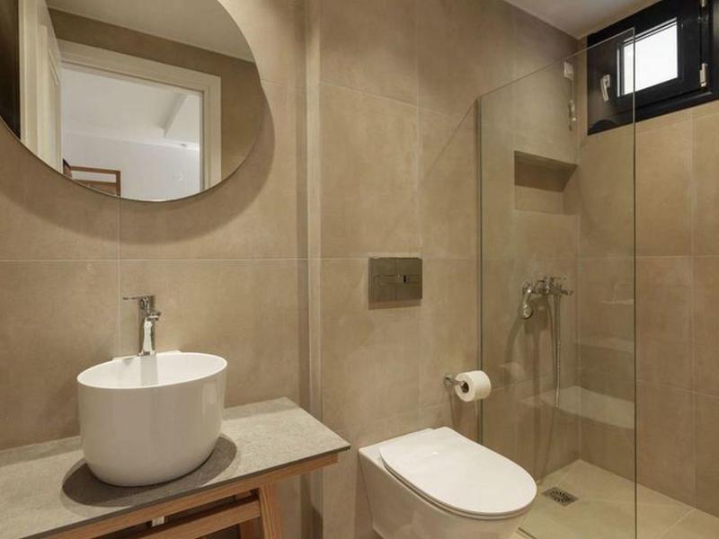 Modern bathroom with round mirror, sink, and glass-enclosed shower.