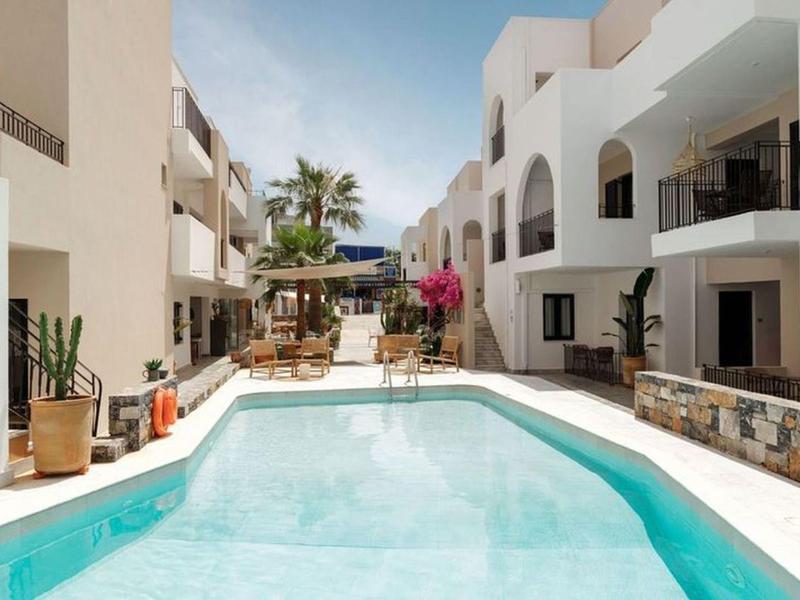 Modern hotel pool area with sun loungers and white building under sunny weather.