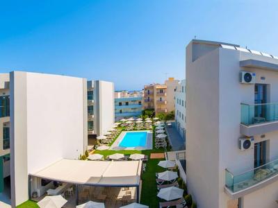 Blick auf einen modernen Hotelkomplex mit Pool und Liegestühlen unter klarem Himmel.