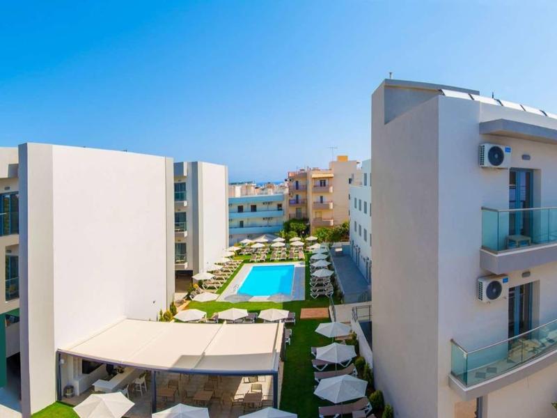 Modern hotelcomplex met zwembad, witte gebouwen en parasols onder een heldere lucht.