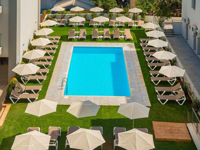 Rechthoekig zwembad met ligstoelen en parasols in een hotel tuin.