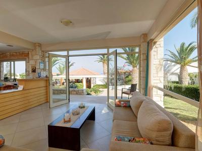 Lounge luminosa con divano e vista sul giardino con palme e gazebo.