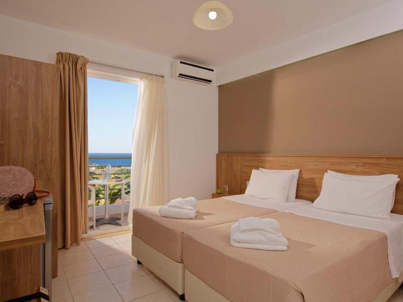 Chambre d'hôtel avec deux lits simples, balcon et vue sur la mer, espace lumineux et accueillant.