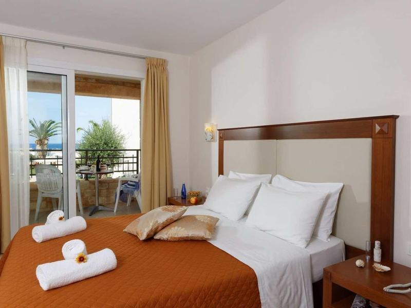 Chambre d'hôtel moderne avec lit double, balcon et vue sur des palmiers.