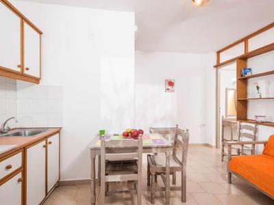 Piccola cucina con armadietti in legno, tavolo da pranzo e divano arancione in stanza luminosa.