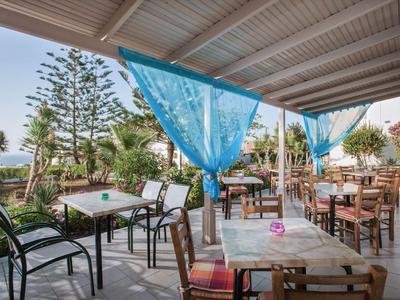 Terrazza esterna coperta con tavoli, sedie e tende blu in un giardino dell'hotel.