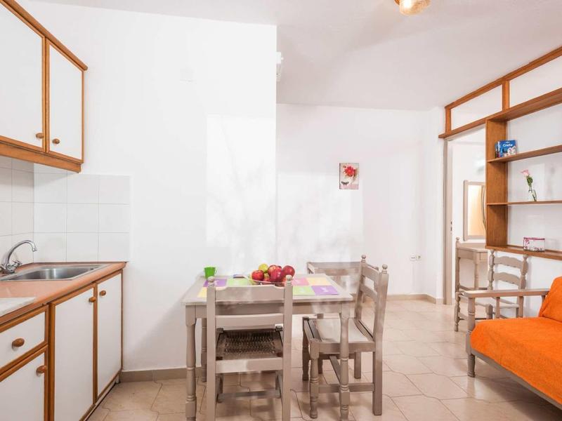 Petit coin repas avec table en bois, chaises et canapé orange dans une cuisine lumineuse.