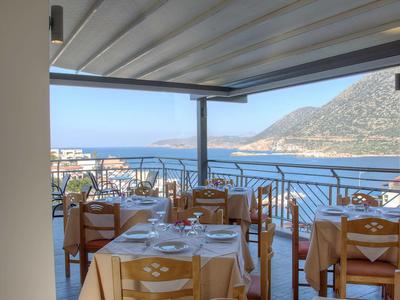 Überdachte Terrasse eines Restaurants mit Blick auf das Meer und Berge im Hintergrund.