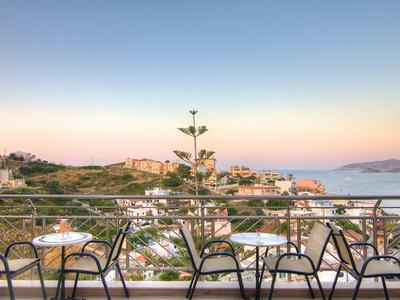 Balkon mit Tischen und Stühlen bietet Blick auf Küste und Meer bei Sonnenuntergang.