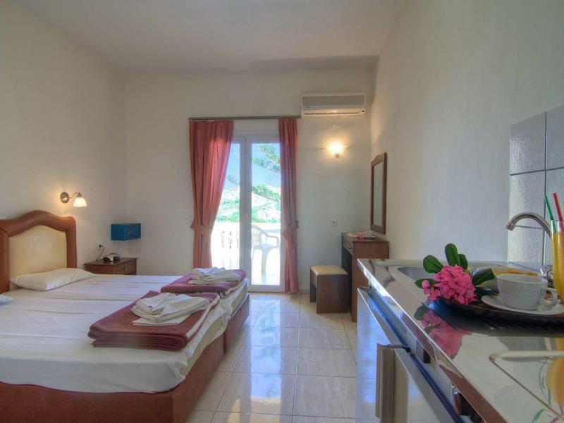 Helles, einfaches Hotelzimmer mit Doppelbett, Balkon, Klimaanlage und Minibar in warmen Farbtönen.