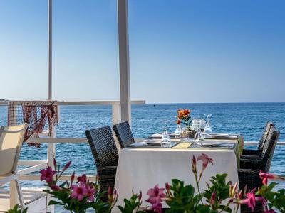 Tavolo in terrazza con tovaglie bianche e vista mare in una giornata di sole.