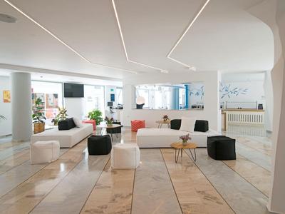 Area lounge moderna e luminosa in hotel con mobili bianchi e piante.