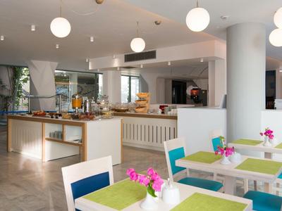 Ristorante moderno e luminoso con tavoli apparecchiati, fiori e area buffet.