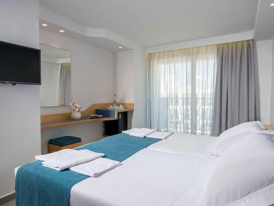 Chambre d'hôtel moderne avec deux lits simples, bureau, télévision et balcon avec rideaux.