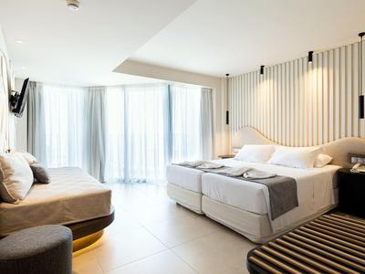 Chambre d'hôtel moderne avec lit double, banc, chaise et grands rideaux à la fenêtre.