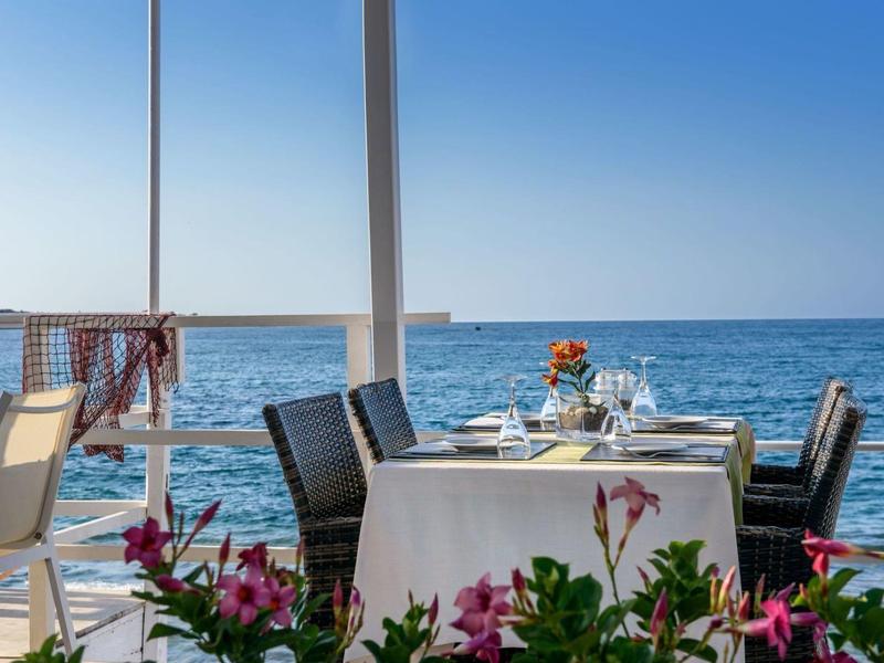 Table de terrasse avec nappes blanches et vue sur la mer par une journée ensoleillée.