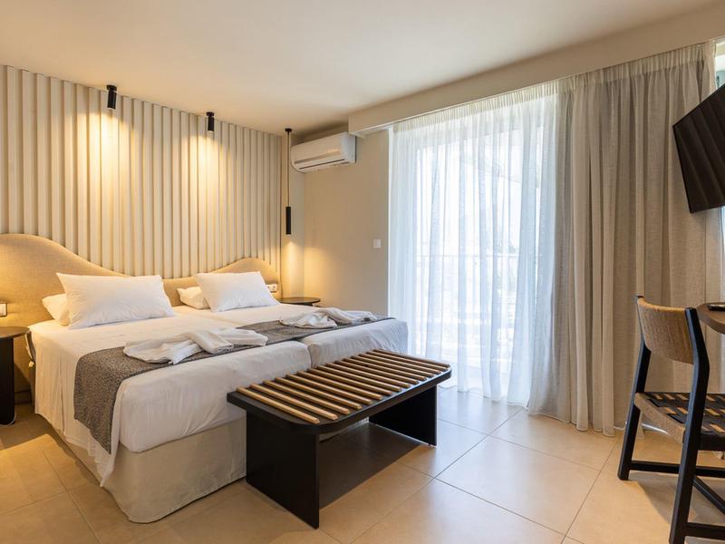 Chambre d'hôtel moderne avec lit double, banc, téléviseur et grande fenêtre avec rideaux.