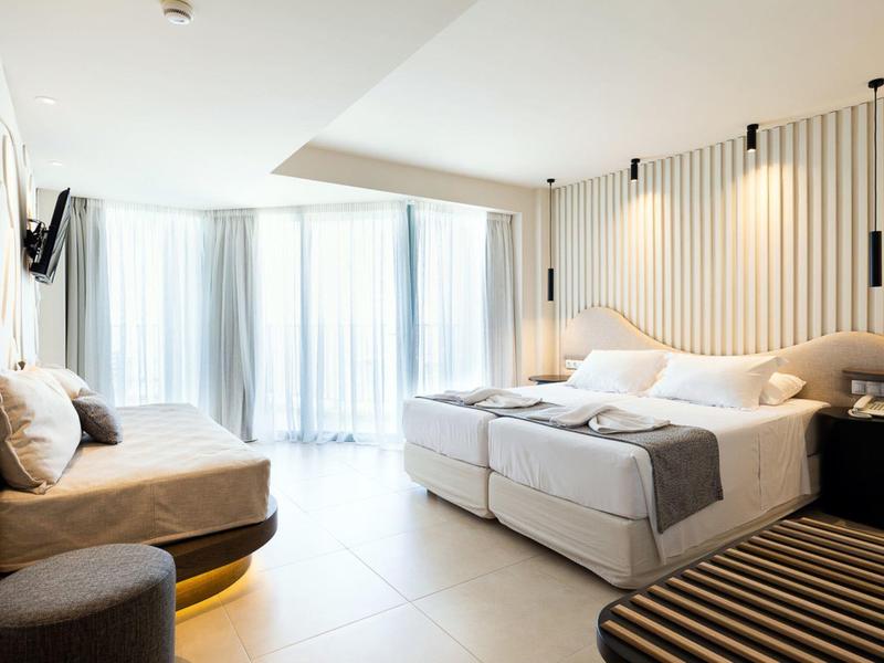 Chambre d'hôtel moderne avec lit double, banc, chaise et grands rideaux à la fenêtre.