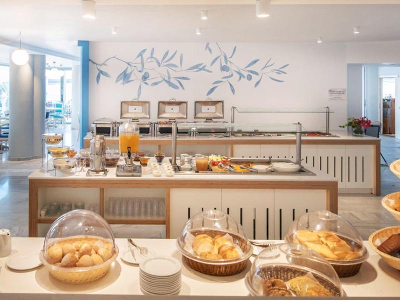 Buffet avec diverses pâtisseries, jus et machines à café dans une salle à manger lumineuse.