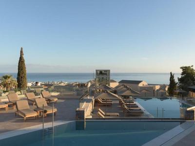 Hotel pool with lounge chairs and sea view under clear sky.